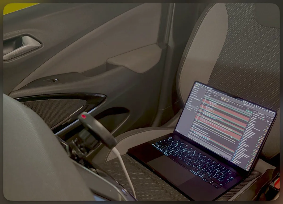 An open MacBook running several coding-agent sessions on the passenger seat of my car, plugged into a power cable before a 45-minute drive to a client.